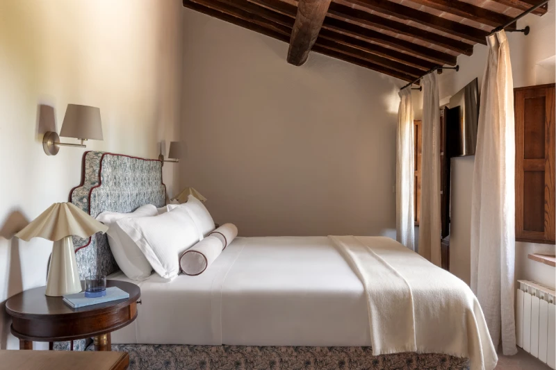 Double bed beneath a beamed ceiling, round bedside tables and warm light, an elegant rustic room near Asciano - Villa San Barolomeo, BZAR hotels in Tuscany