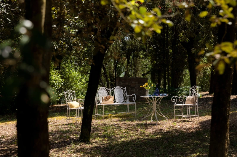 Shaded garden lounge with white wrought-iron seating and table, ideal for relaxing stays in the Crete Senesi countryside - Villa San Barolomeo, BZAR hotels in Tuscany