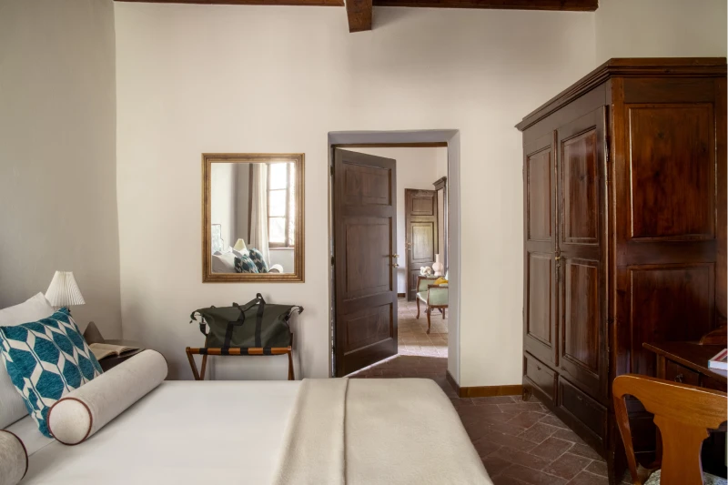 Bedroom with white bed, antique wardrobe and doorway to the living room, authentic spaces for holidays near Asciano - Villa San Barolomeo, BZAR hotels in Tuscany