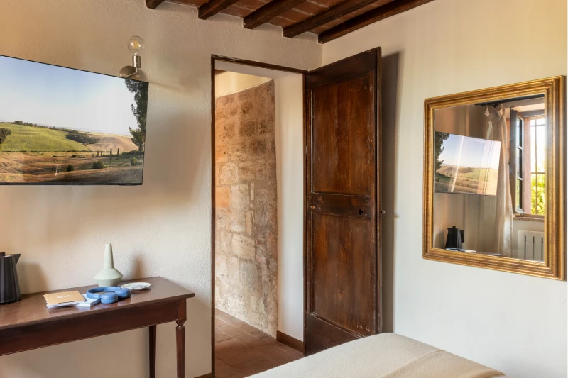 Bedroom with TV, gilded mirror, wooden door and beamed ceiling, authentic comfort in the Crete Senesi - Villa San Barolomeo, BZAR hotels in Tuscany