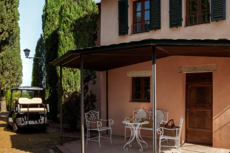Outdoor patio with white iron table, pink facade, cypress trees and golf cart, villa relaxation near Asciano - Villa San Barolomeo, BZAR hotels in Tuscany