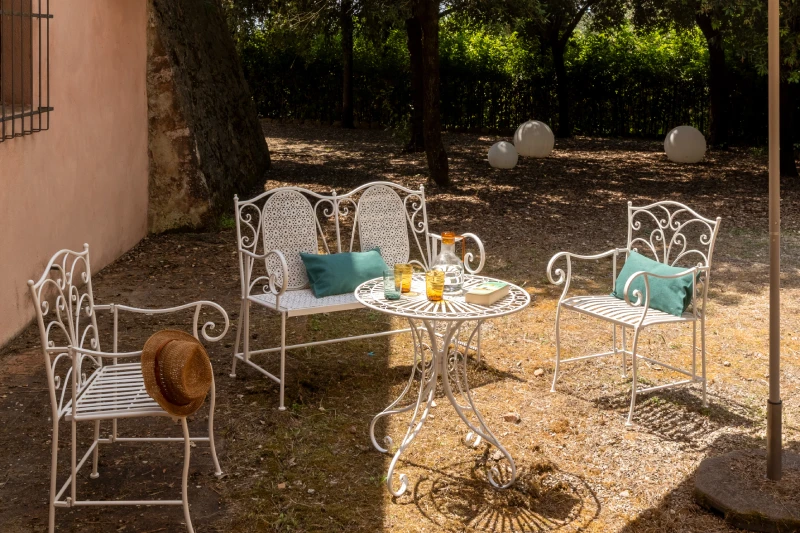 Garden relaxation area with white iron seating, blue cushions and small table, quiet moments in the Crete Senesi - Villa San Barolomeo, BZAR hotels in Tuscany