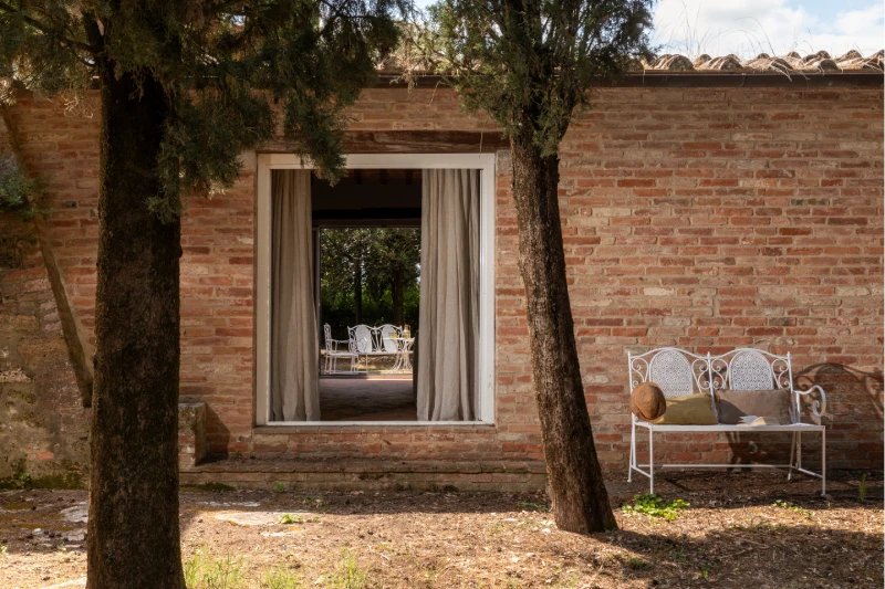 Brick facade with large garden opening and wrought-iron bench, rustic Tuscan charm in the landscape around Asciano - Villa San Barolomeo, BZAR hotels in Tuscany