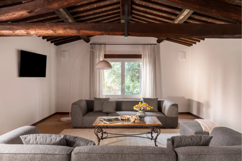 Spacious living room with grey sofas, exposed wooden beams and natural light, elegant comfort in a villa near Asciano - Villa San Barolomeo, BZAR hotels in Tuscany