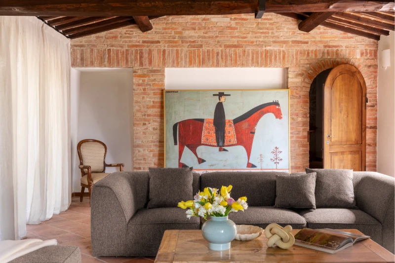 Living room with brick wall, grey sofa and large decorative artwork, rustic design for a Tuscan countryside holiday - Villa San Barolomeo, BZAR hotels in Tuscany