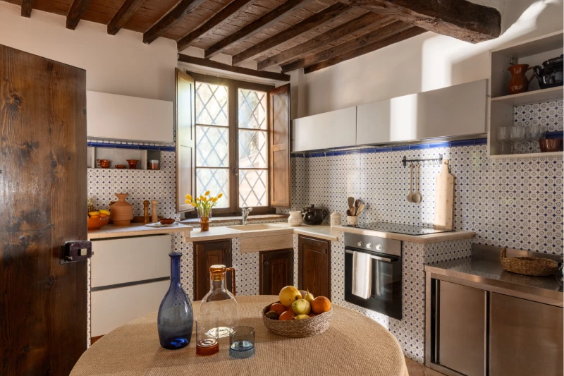 Tuscan kitchen with blue and white tiles, wooden beams and round dining table, holiday apartment near Asciano - Villa San Barolomeo, BZAR hotels in Tuscany